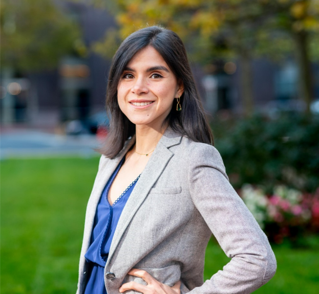 Equal Justice Works Fellow Claudia Torres Patino poses in a gray suit and blue blouse in front of a green lawn