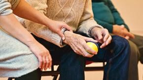 Close up picture of a young woman's hand resting on an elderly man's arm as the man holds a tennis ball.