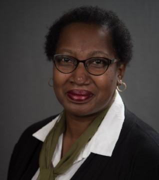 Executive Director Jacquelynne J. Bowman is wearing a white shirt and dark jacket. She is seated in front of a dark gray background.