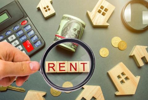 image of a table with wooden houses a calculator and a magnifying glass showing a rent word